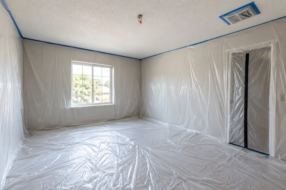 Empty bedroom sealed in plastic with a zipper door and a taped-over ceiling vent